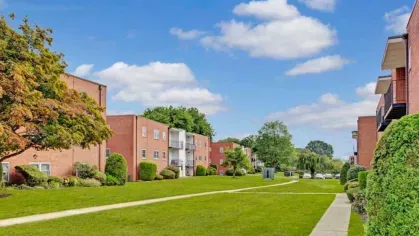 A pathway leading through a green courtyard with multiple red brick apartment buildings on either side.