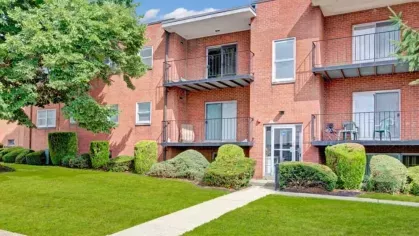 A close-up of a red brick apartment building with balconies and trimmed bushes.
