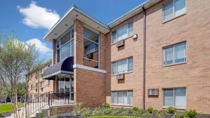 Exterior of a brick apartment building with large windows and a dark awning entrance.