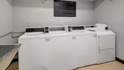 A laundry room featuring several white washers and dryers along with a set of laundry room rules displayed above.