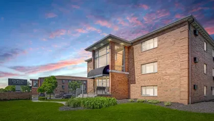 A brick apartment building at sunset, highlighted by vibrant skies and lush greenery in the foreground.