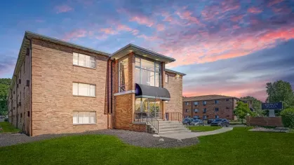 Another angle of a brick apartment complex during sunset, showcasing a welcoming entrance and a view of the parking area.