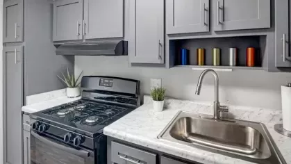 A modern kitchen with gray cabinets, marble countertops, and a sleek gas stove.