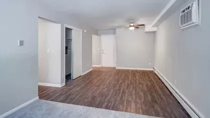 A large, empty living space with wood floors, a ceiling fan, and natural light from a window.
