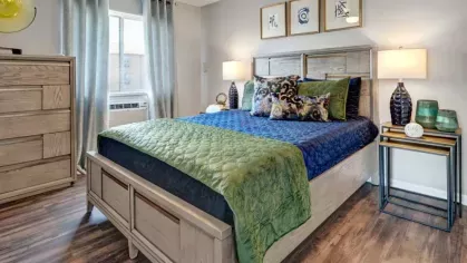 A stylish bedroom with a wooden bed frame, green and blue bedding, and matching decor.