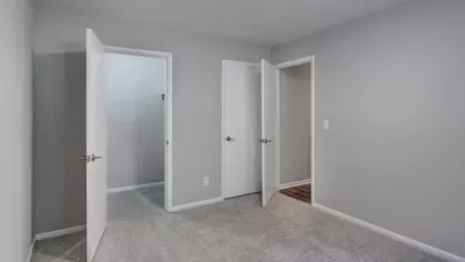 A simple, neutral-toned bedroom with open doors revealing adjacent spaces.
