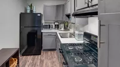 A compact kitchen with dark gray cabinets, marble countertops, and modern appliances.