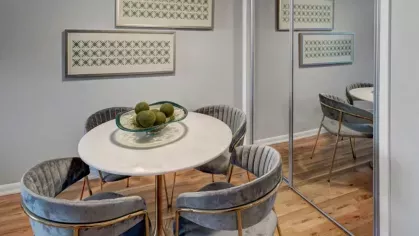  A dining area featuring a round table, four velvet chairs, and mirrored accents on the wall.