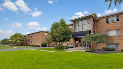 A brick apartment building with large glass windows and a well-maintained green lawn.