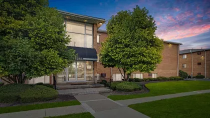 A twilight view of a brick apartment building surrounded by manicured lawns and mature trees.