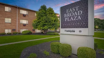 The East Broad Plaza Apartments sign set against a backdrop of a well-maintained lawn and a colorful sunset.