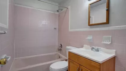 Bathroom with a pink-tiled bathtub, white sink, and a wooden cabinet for a retro-inspired design.
