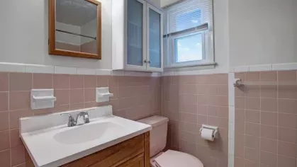 A small bathroom featuring a pink tiled design, wooden vanity, and bright window.