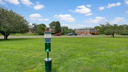 A pet dog waste station on a spacious grassy expanse near a parking area.