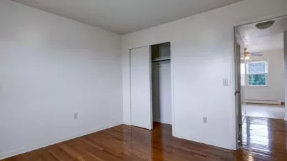 Bright bedroom featuring a closet, white walls, and a connection to the rest of the apartment.