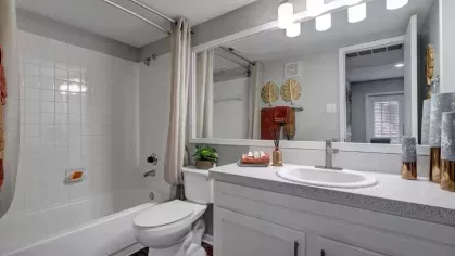 A contemporary bathroom with white tiles, a large mirror, and decorative accents on the countertop.