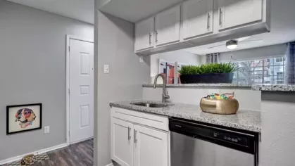 A modern kitchen featuring white cabinets, granite countertops, and stainless steel appliances with a view of the living area.