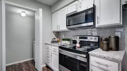 A cozy kitchen with white cabinetry, a sleek microwave, and a granite countertop leading to a laundry room.