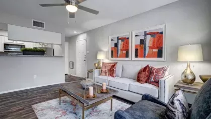 A modern living room with a ceiling fan, artistic wall art, and a mix of vibrant and neutral furnishings.