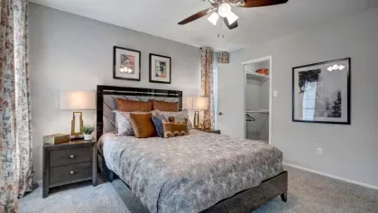 A well-decorated bedroom with a ceiling fan, plush bedding, and a walk-in closet in the background.