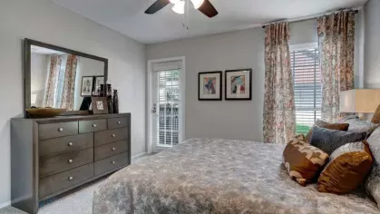 A bedroom with a large dresser, patterned curtains, and access to a private patio through glass doors.