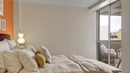 A serene bedroom setup with light-toned bedding and a balcony view.