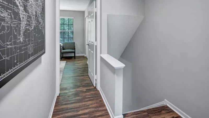 A hallway with wood flooring, a world map decor, and a view into a room with large windows.