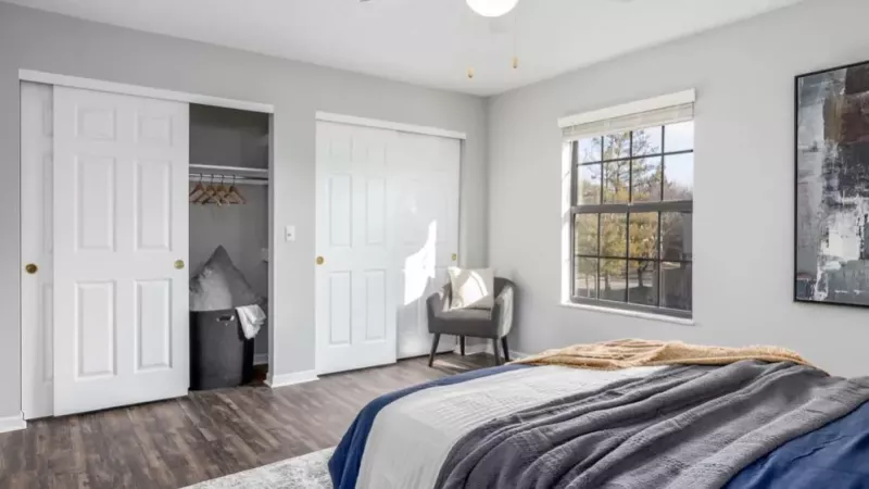 A spacious bedroom with sliding closet doors, a large window, and an inviting reading chair.
