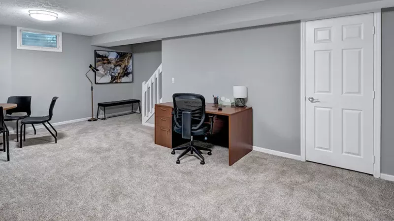 A spacious basement area with a desk setup, comfortable seating, and soft carpeting throughout.