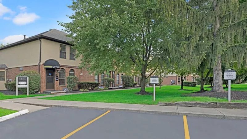 The exterior of the leasing office building surrounded by well-maintained landscaping and trees.