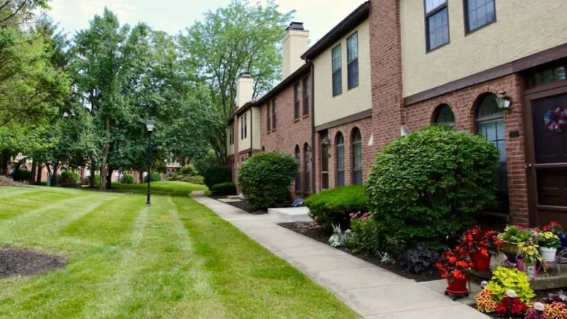 A landscaped walkway with neatly trimmed bushes and vibrant flowers leading to a row of brick townhomes.