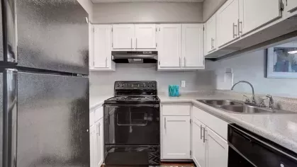  A modern kitchen featuring white cabinets, granite countertops, and stainless steel appliances with a view of the living area.