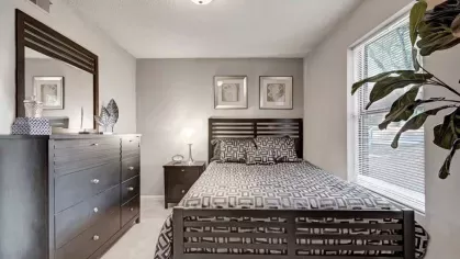 A bedroom with a dark wood bed and dresser, adorned with black-and-white patterned bedding and large windows.