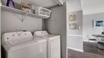 A compact laundry area with a washer and dryer under open shelving stocked with cleaning supplies.