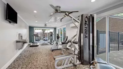 A modern fitness center with cardio machines, weight training equipment, and large windows for natural light.