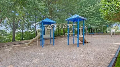A colorful playground surrounded by lush greenery, featuring slides and climbing structures.