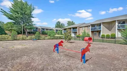 A small pet park featuring red horse-shaped seesaws and a fenced-in area with nearby apartments.