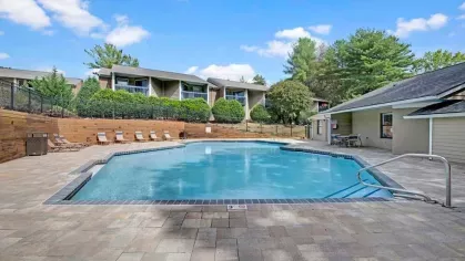 A crystal-clear swimming pool with paved surroundings and cozy seating, nestled among residential units.