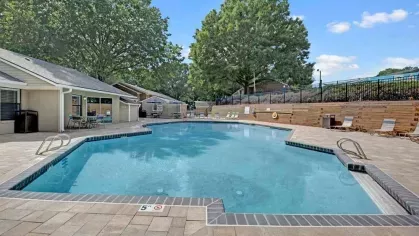 Another angle of the swimming pool area, showcasing a spacious patio and shaded community amenities.