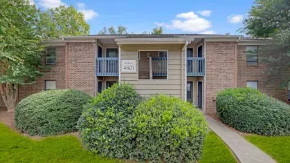 A residential building with balconies and lush greenery in the front.