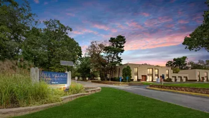 A scenic view of Mill Village Apartments' sign at sunset, surrounded by greenery and vibrant skies.
