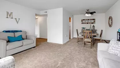 An open-plan living and dining area with neutral-toned furnishings and a ceiling fan.