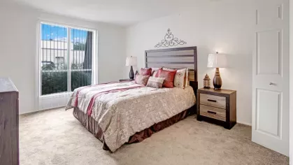 A serene bedroom with a large window, a patterned bedspread, and minimalist furniture.