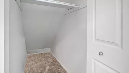 A spacious walk-in closet with carpet flooring and a white finish.