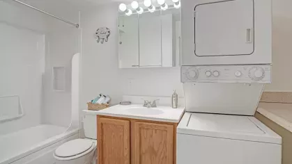 A bathroom featuring a bathtub, sink, and an in-unit stacked washer and dryer.