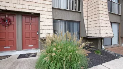 An exterior view of the apartments with a red door, beige siding, and landscaped greenery.