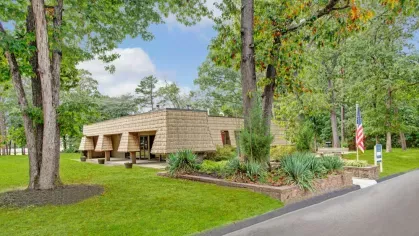 a charming building surrounded by lush greenery and mature trees, featuring a U.S. flag and vibrant landscaping.