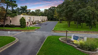 a community entrance, complete with a sign for "Mill Village Apartments" and a welcoming landscaped area at twilight.