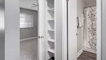 A hallway with a linen closet and adjacent bathroom featuring floral patterned curtains.