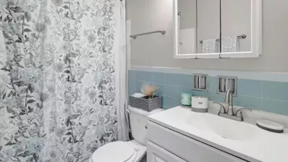 A bathroom with blue and floral tile accents, a vanity mirror, and a bright shower curtain.